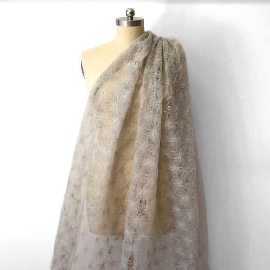 EOS Fabrics shimmering snowflake tulle in smoke gray with metallic gold accents draped on a dress form