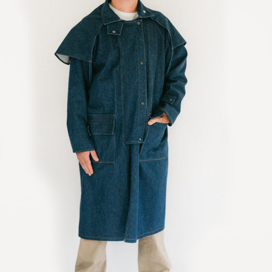 Man standing in front of a white screen wearing a dark blue Drover's Coat.