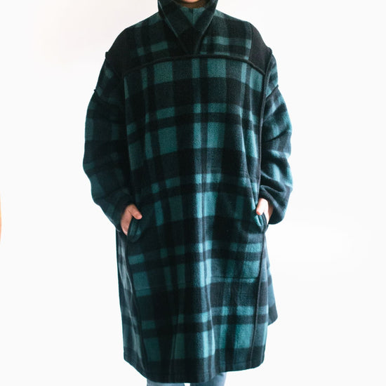 Photo of young woman wearing parka with hood pulled up.  hands are in both pockets and she looks forward towards the camera.