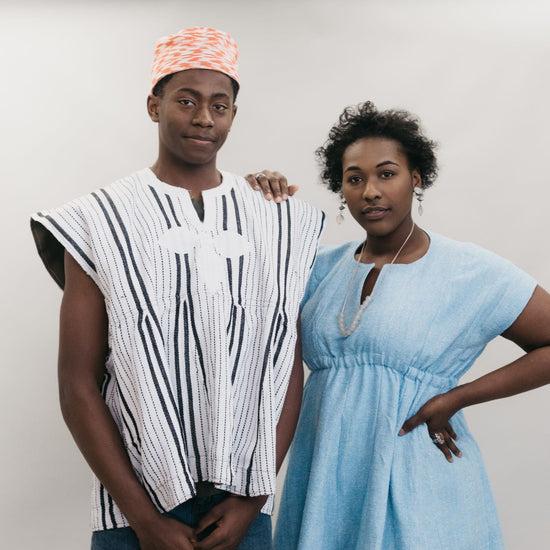 An African American young man and women standing in front of a white studio backdrop wearing the Ghanaian Smock.