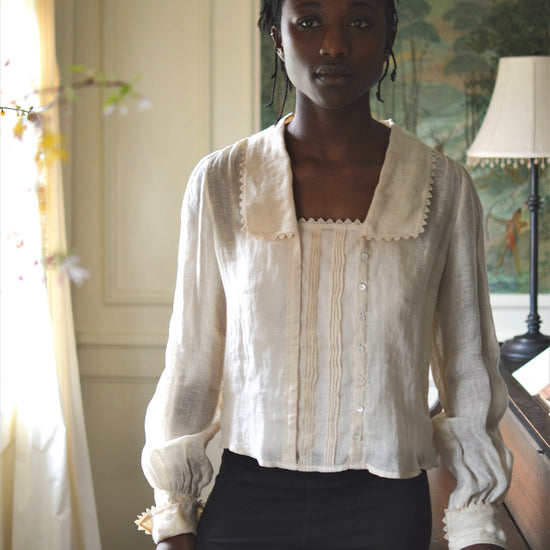 African woman standing in a room beside a piano wearing 210 Armistice Blouse and black leggings.