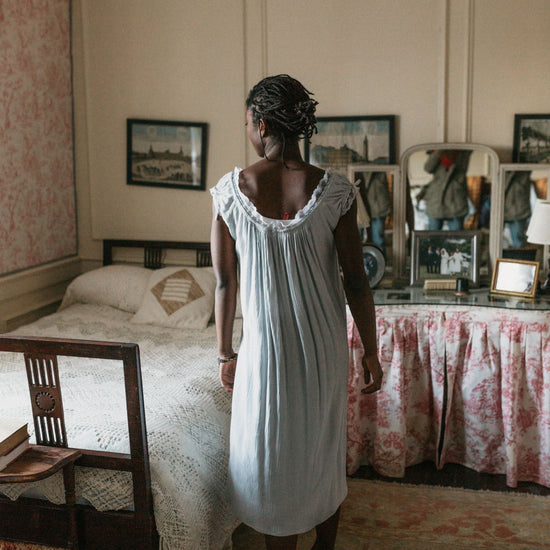 Back view of African women standing next to a bed wearing 223 A Lady's Chemise.