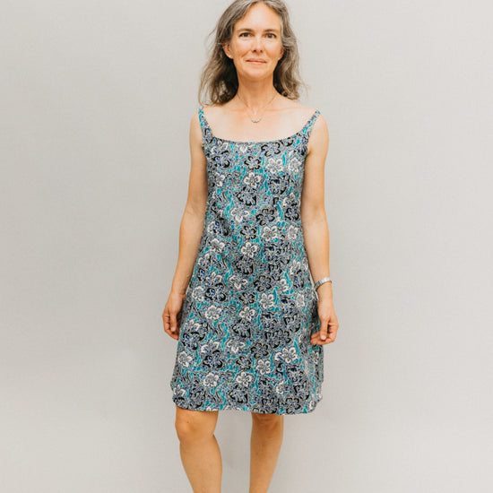 Woman wearing a teal, white, and black floral knee-length dress with narrow straps.