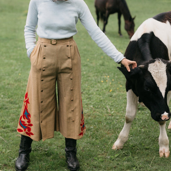 Woman wearing 231 Big Sky Riding Skirt buttoned to the right for a pants effect petting a black and white cow.