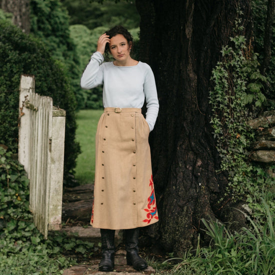 Woman standing in front of an open gate surrounded by greenery wearing the 231 Big Sky Riding Skirt buttoned to the left for a skirt effect.