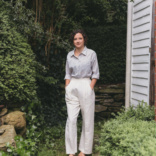 Young brunette white woman walking surrounded by greenery, wearing the Rosie the Riveter slacks and shirt.