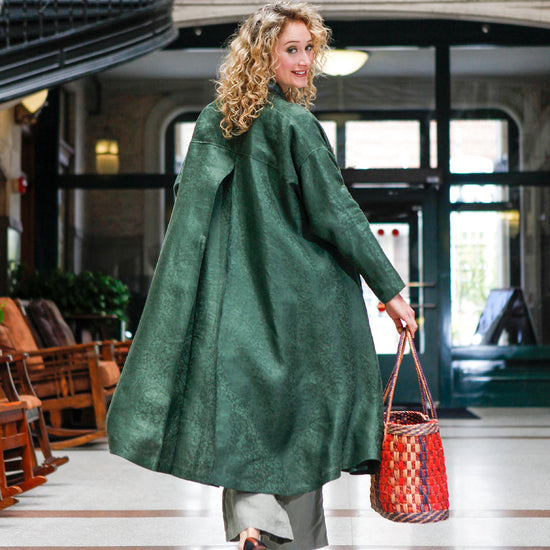 Back view of a blonde white woman looking over her shoulder holding a woven purse wearing 254 Swing Coat open.