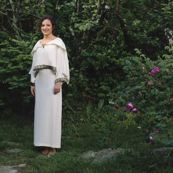 Young Brunette White woman wearing the #266 Greek Island Dress with Jacket in white standing surrounded by Greenery.