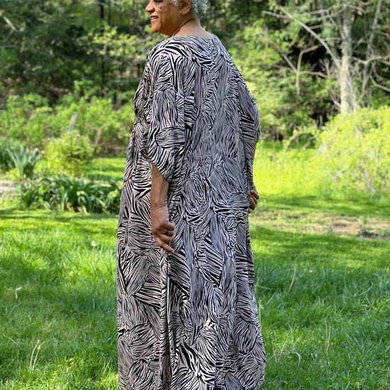 Woman standing outside wearing a pink and black patterned kaftan.  Her back is toward the camera.