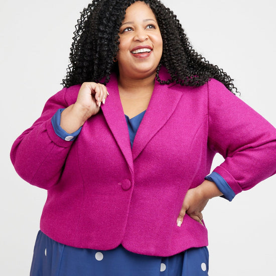 Woman wearing a bright pink blazer over a blue dress with white polka dots on a white background. This blazer is the Auburn Blazer sewing pattern from Cashmerette.