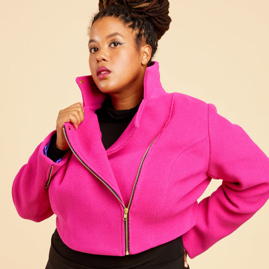 Person wearing a bright pink jacket and black pants on a beige background. This biker jacket is the Canton Moto Jacket sewing pattern from Cashmerette.