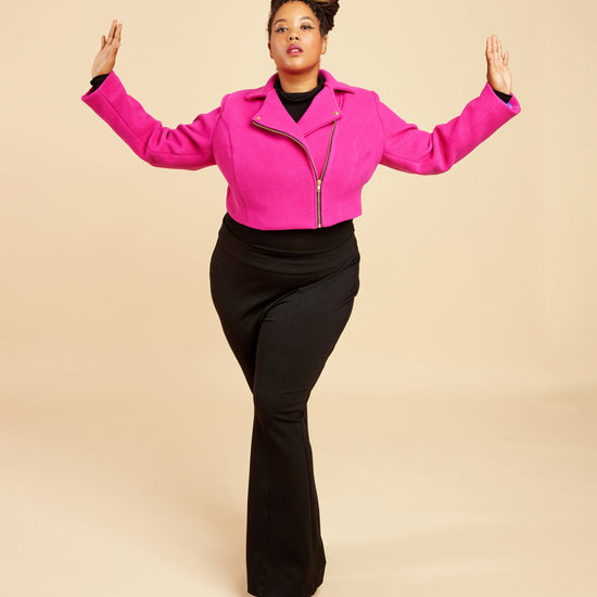 Person wearing a bright pink jacket and black pants on a beige background. This biker jacket is the Canton Moto Jacket sewing pattern from Cashmerette.