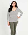 A woman standing, wearing a striped long-sleeved t-shirt and green pants. This t-shirt is the Concord T-Shirt sewing pattern from Cashmerette.