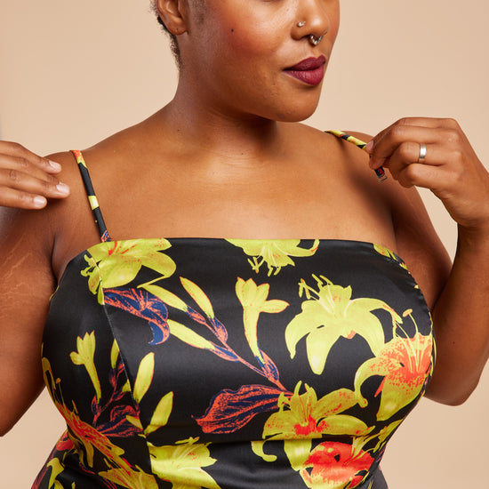 Woman wearing a black dress with colorful floral patterns on a beige background. This dress is the Ellington Strapless Dress sewing pattern from Cashmerette.
