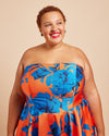 Woman wearing a strapless dress with blue floral pattern on a beige background. This dress is the Ellington Strapless Dress sewing pattern from Cashmerette.