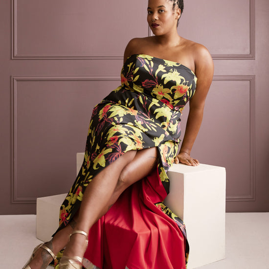 Woman in a floral strapless dress sitting on a white cube against a purple wall. This dress is the Ellington Strapless Dress sewing pattern from Cashmerette.