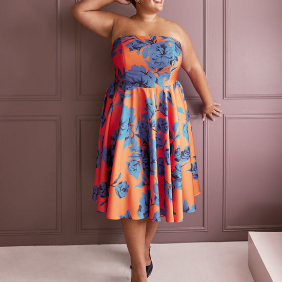 Woman wearing a strapless dress with blue floral pattern against a pink paneled wall. This dress is the Ellington Strapless Dress sewing pattern from Cashmerette.