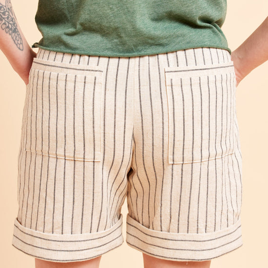 Beige shorts with black stripes worn by a person on a beige background. These shorts are the Everett Pants & Shorts sewing pattern from Cashmerette.