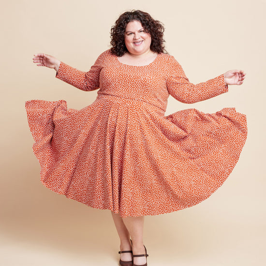 Woman wearing an orange patterned dress on a beige background. This is the Grafton Dress, Top & Skirt sewing pattern from Cashmerette.