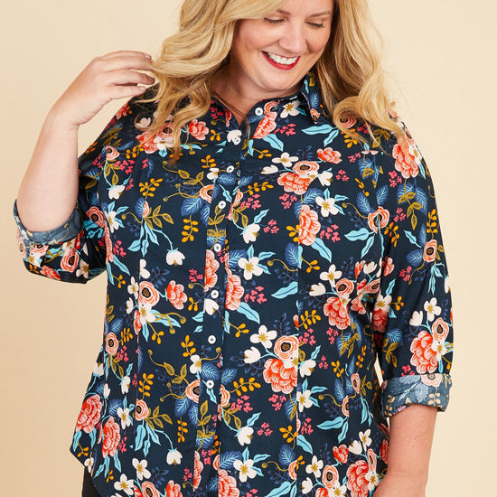 Woman wearing a floral blouse on a beige background. This button-up shirt is the Harrison Shirt sewing pattern from Cashmerette.