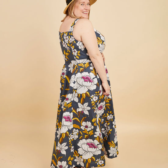 Woman wearing a floral dress and straw hat on a beige background. This is the Holyoke Maxi Dress & Skirt sewing pattern from Cashmerette.