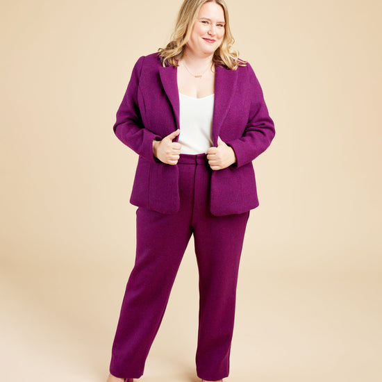 Woman wearing a purple suit on a beige background. These pants are the Meriam Trousers sewing pattern from Cashmerette.