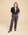 Woman wearing a black blouse with a white bow and patterned pants on a beige background. These pants are the Meriam Trousers sewing pattern from Cashmerette.