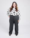 Woman wearing a polka dot blouse and gray pants on a white background. These pants are the Meriam Trousers sewing pattern from Cashmerette.