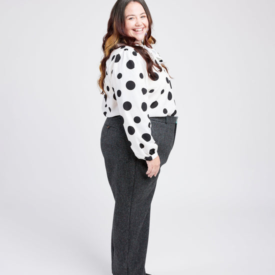 Woman wearing a polka dot blouse and gray pants on a white background. These pants are the Meriam Trousers sewing pattern from Cashmerette.