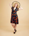 Woman wearing a patterned dress and wide-brimmed hat on a beige background. This dress is the Roseclair Wrap Dress sewing pattern from Cashmerette.