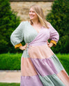 Woman wearing a colorful dress with a green, pink, and purple pattern standing outdoors.This dress is the Roseclair Wrap Dress sewing pattern from Cashmerette.
