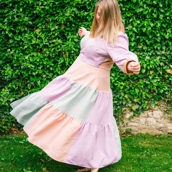 Woman in a pastel-colored dress twirling in front of a green hedge.. This dress is the Roseclair Wrap Dress sewing pattern from Cashmerette.