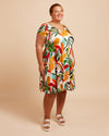 Woman wearing a colorful tropical print dress on a beige background