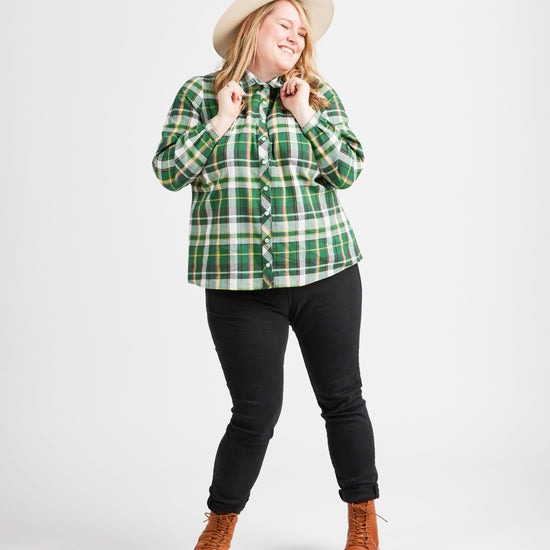 Woman wearing a green plaid shirt, black pants, and brown boots on a white background. This top is the Vernon Shirt sewing pattern from Cashmerette.