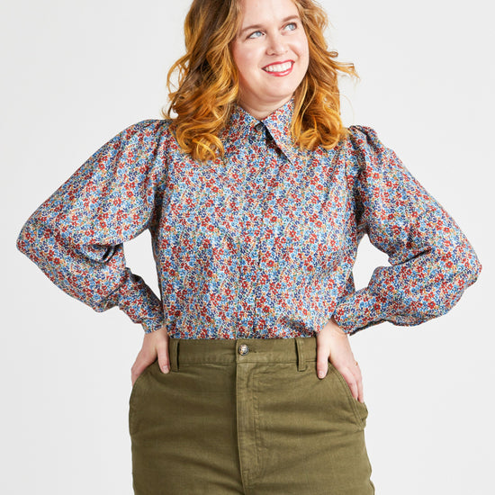Woman wearing a floral blouse and green pants against a plain background. This top is the Vernon Shirt sewing pattern from Cashmerette.