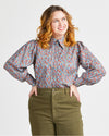 Woman wearing a floral blouse and green pants against a plain background. This top is the Vernon Shirt sewing pattern from Cashmerette.