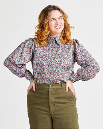 Woman wearing a floral blouse and green pants against a plain background. This top is the Vernon Shirt sewing pattern from Cashmerette.