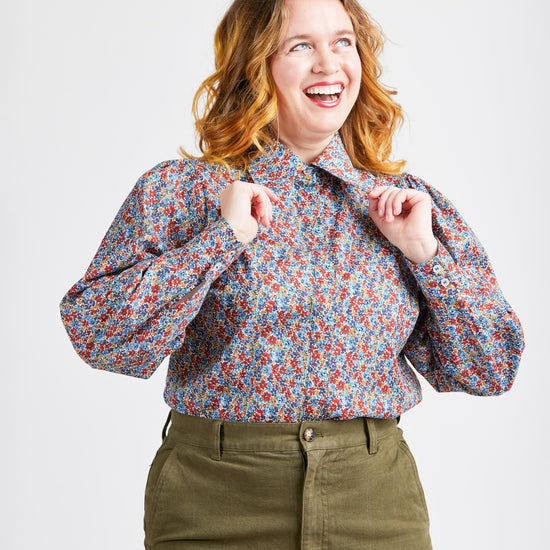 Woman wearing a floral blouse and green pants on a white background. This top is the Vernon Shirt sewing pattern from Cashmerette.