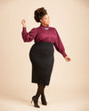 Woman wearing a burgundy blouse and black skirt on a beige background. This top is the Vernon Shirt sewing pattern from Cashmerette.