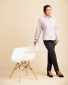 Woman in a light purple shirt and dark pants standing next to a white chair on a beige background. This top is the Vernon Shirt sewing pattern from Cashmerette.