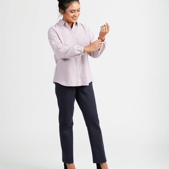 Woman wearing a light pink blouse and dark pants on a white background. This top is the Vernon Shirt sewing pattern from Cashmerette.